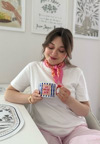 Mug in ceramica con strisce blu e manico rosso, con la scritta "LA DOLCE VITA" su sfondo bianco. Sciarpa rosa, t-shirt bianca e pantaloni a quadri rosa.
