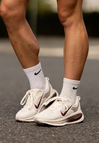 Bijele Nike sportske cipele s tamnocrvenim detaljima, površinom od teksturirane mreže i udobnim đonom. Uparen s bijelim sportskim čarapama koje imaju crni logo.