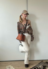Randig långärmad skjorta, vita texturerade stickade byxor, brun mockaväska med läderdetaljer och en beige keps. Mörka skor fulländar looken.