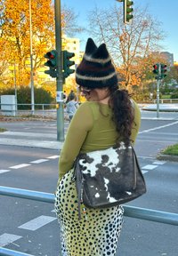 Tas met koeienhuidpatroon, een bruine leren basis en een decoratieve bedel; gecombineerd met een aansluitende olijfgroene top en een patroonrok.