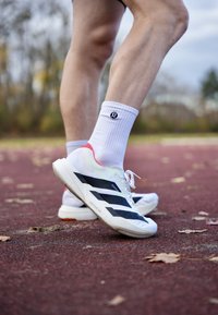 Valged spordijalatsid mustade triipudega, kontsal roosad aktsendid, valgete sokkidega, paigutatud punasel jooksurajal koos langenud lehtedega.