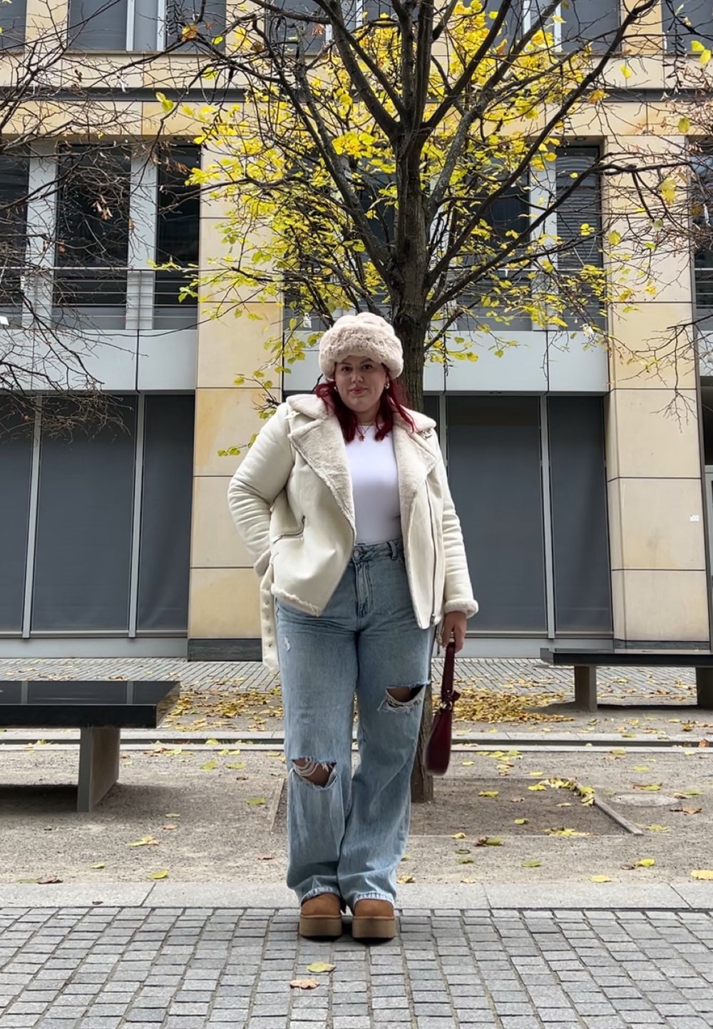 Λευκή γούνα πάνω από λευκή μπλούζα, ανοιχτό μπλε χαλαρές τζιν, μπεζ πλατφόρμες και κρέμα καπέλο, στέκεται σε εξωτερικό χώρο.