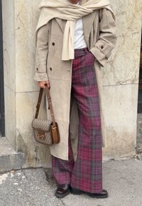 Manteau en daim beige, pull blanc, pantalon large à carreaux dans des nuances de rose et de violet. Sac à main marron avec un devant à motifs. Chaussures sombres.