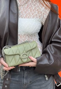 Šviesiai žalia siuvinėta odinė rankinė su sidabriniu grandinėlės dirželiu ir sagtimi. Parodo kompaktišką stačiakampį formą ir ryškų siuvimo detalę.