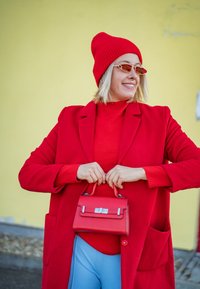 Κόκκινο μάλλινο παλτό, κόκκινο πλεκτό σκουφί, κόκκινα γυαλιά ηλίου και μια μικρή κόκκινη τσάντα με ασημί αξεσουάρ, συνδυασμένα με ανοιχτό μπλε παντελόνι.