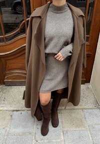 Palton maro din lână peste un pulover și fustă gri, asortat cu cizme maro din piele întoarsă până la genunchi. Țesătură texturată, manșete cu dungi și design ajustat.