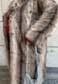 Manteau en fausse fourrure dans des tons bruns et gris avec des manches longues, accompagné d'un petit sac à main en maille argentée avec une bandoulière perlée.