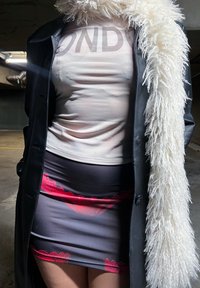 Femme portant un manteau en cuir noir avec une bordure en fourrure blanche, un t-shirt beige Bonds et une mini-jupe noire avec des détails en dentelle rouge dans un parking sombre.