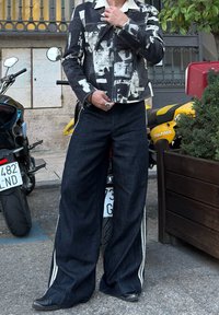 Black and white printed jacket with a collared neckline, paired with wide-leg dark denim jeans featuring side stripes and black shoes.