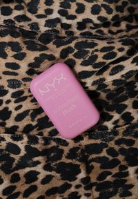 NYX Buttermelt Blush i pink oval kompakt, med hvid tekst. Placeret på et leopardmønster stof med en tan- og sort farveskala.
