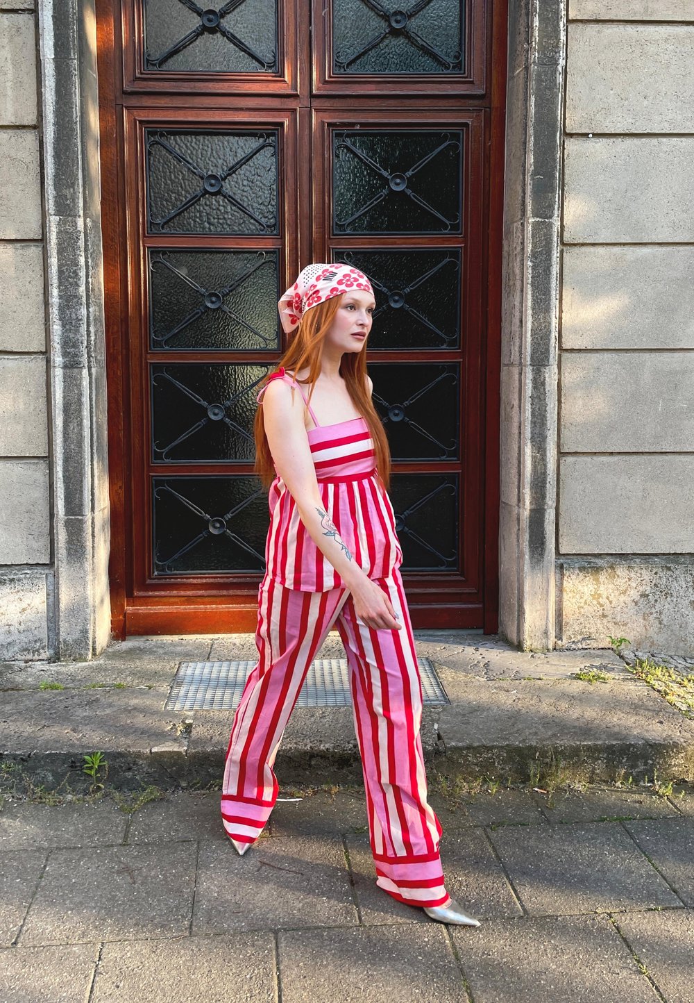 Sarkans un balts svītrots kombinezons ar kvadrātveida dekoltē, sasiets siksnas un brīvs piegriezums. Saskaņots ar ziedu raksta galvas lakatu un sudraba papēžiem.