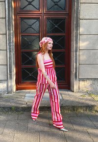 Sarkans un balts svītrots kombinezons ar kvadrātveida dekoltē, sasiets siksnas un brīvs piegriezums. Saskaņots ar ziedu raksta galvas lakatu un sudraba papēžiem.