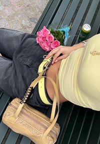 Keltainen toppi, mustat korkea vyötäröiset housut, keltainen vyö ja beige käsilaukku, jossa on tekstuuripinta. Lähistöllä pinkki ruusukimppu.