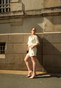 Ensemble deux pièces beige clair composé d'un haut à manches courtes et d'un short assorti, avec un détail de logo. Des talons aiguilles complètent l'ensemble.