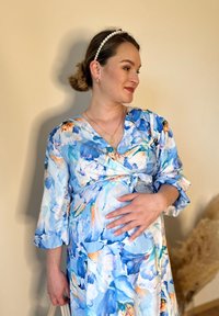 Φλοράλ φόρεμα με νηματοποίηση σε ανοιχτό μπλε χρώμα με πολύχρωμα λουλουδάτα μοτίβα. Έχει μακριά μανίκια και ζωνάκι που δένει, συνδυασμένο με ένα περιφούρνιστο κεφαλοτύλι.