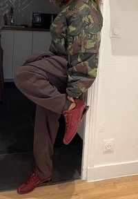 Casaco bomber camuflado, calças largas castanhas e ténis Nike Air Max vermelhos com parte superior texturizada e amortecimento visível de ar.