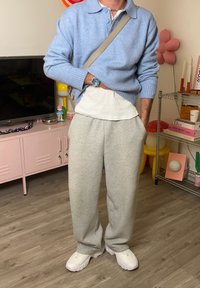 Svetlomodrý sveter, biele tričko a sivé tepláky. Biele tenisky. Doplnky zahŕňajú hodinky a kabelku cez plece. Pohodlný strih.