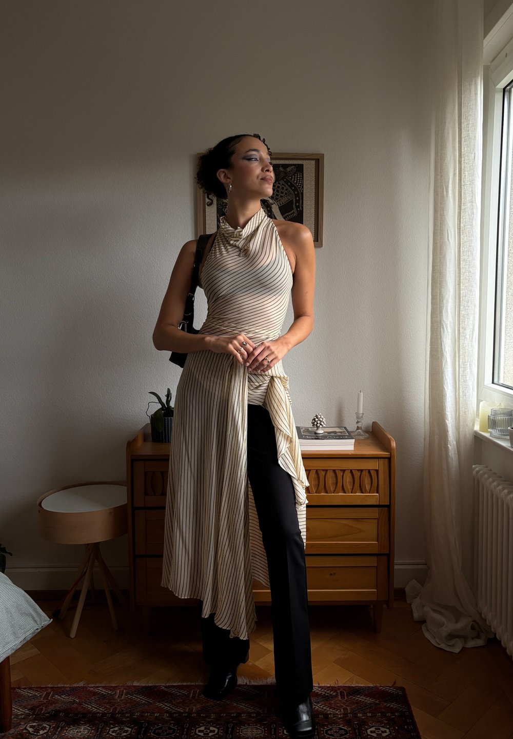 Top fără mâneci, de culoare crem cu dungi fine, având un tiv asimetric, combinat cu pantaloni negri ajustați și cizme negre elegante până la glezne.