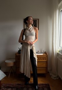 Top fără mâneci, de culoare crem cu dungi fine, având un tiv asimetric, combinat cu pantaloni negri ajustați și cizme negre elegante până la glezne.