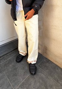 Μαύρο μπουφάν με επένδυση over μια λευκή μπλούζα, συνδυασμένο με παντελόνι σε κρέμα απόχρωση και μαύρες επενδεδυμένες παντόφλες με ανοιχτό καφέ λουριά. Λείος υφές.