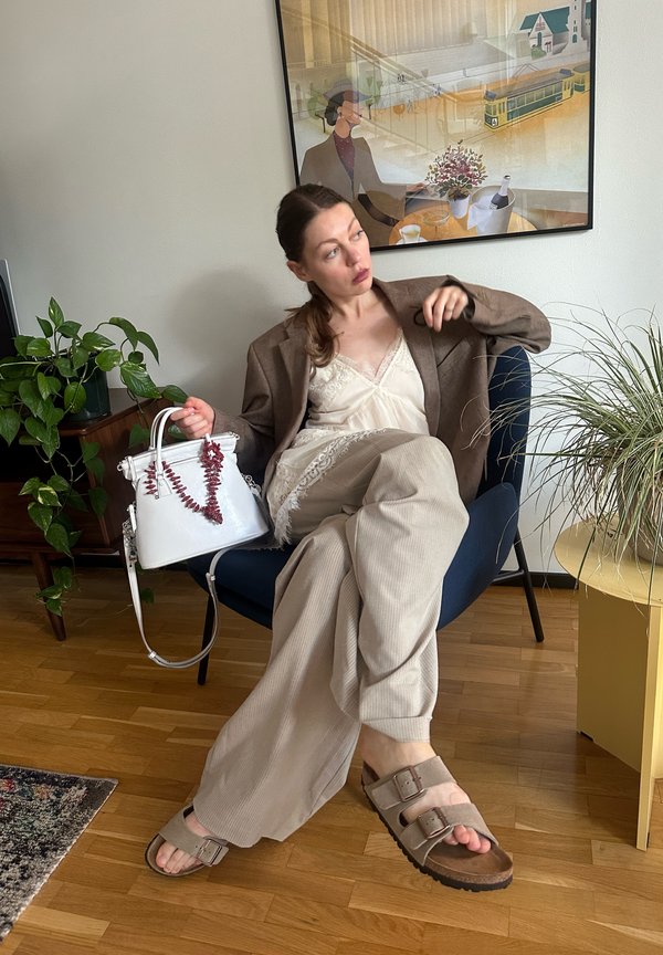 Bela torbica z dekorativnimi koraljnimi dodatki, bež kordne hlače, svetla kamisola, rjav oversized blazer in rjave sandale z dvojnimi trakovi.