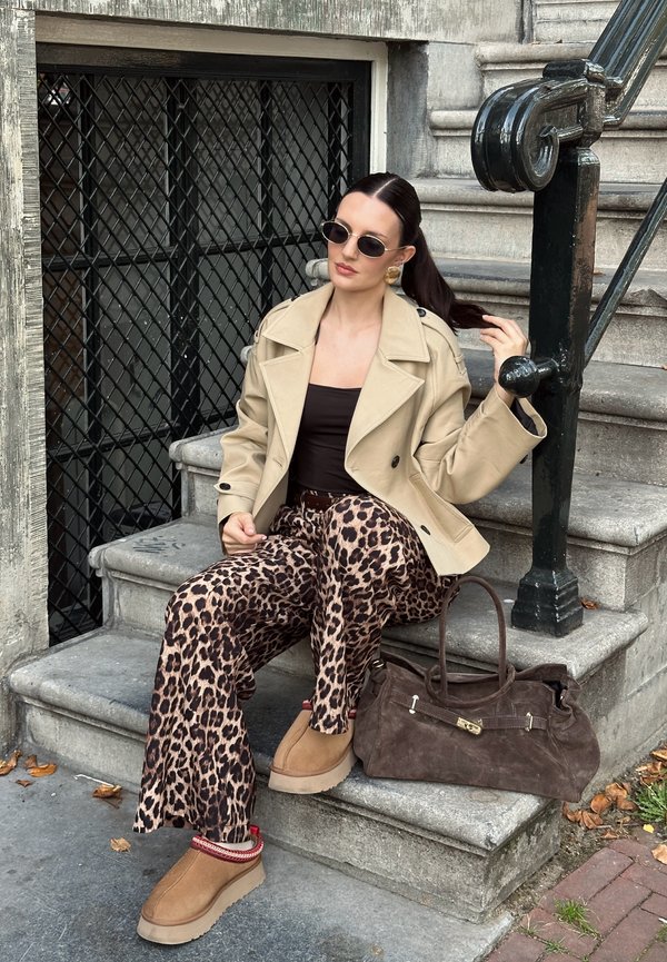 Beige trenchcoat, bruine tanktop, bruine luipaardprint broek, tan fuzzy schoenen, bruine suède handtas, ovale zonnebril, lang donker haar.