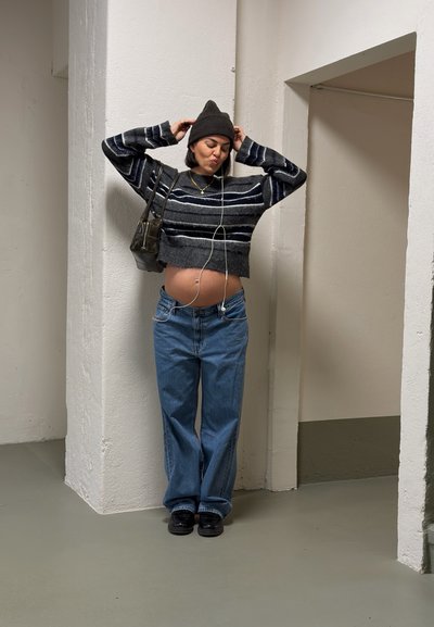 Conjunto informal que incluye un suéter corto de rayas en gris y negro, jeans azules holgados, zapatos negros y un pequeño bolso oscuro.