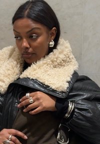 Sort dunjakke med en cremefarvet kunstpelskrave, lagdelt over en mørk top. Sølvringe og creoler tilføjer metalliske accenter.