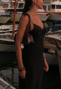 Vestido preto justo com renda, combinado com uma pequena bolsa burgundy. Tecido suave e design minimalista, diante de um fundo de marina.
