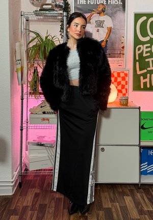 Chaqueta de pelo sintético negra sobre un top corto gris, combinada con una falda negra con rayas blancas laterales y tacones negros. Conjunto casual moderno.