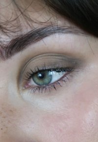 Gros plan sur un œil vert avec des cils bien définis, un maquillage naturel dans des tons neutres et une peau légèrement tachetée de rousseurs autour.
