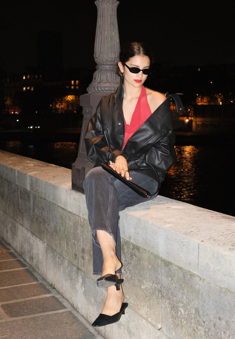 Zwarte leren oversized jas, rode haltertop, grijze cropped jeans en zwarte lage hakken. Elegante zonnebril en een kleine clutch. Nachtsetting.