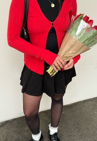 Personne portant un cardigan rouge, une jupe noire et des collants noirs tenant un bouquet de tulipes rouges enveloppé dans du papier kraft.