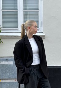 Zwarte oversized blazer gedragen over een witte top, gecombineerd met zwarte losse broeken. Glad materiaal met gestructureerde schouders en zijzakken.