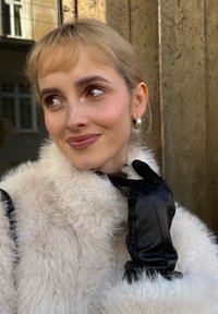 Guantes de cuero negro con acabado suave, usados sobre un abrigo de piel sintética crema y esponjosa, con un cuello alto y tela texturizada.