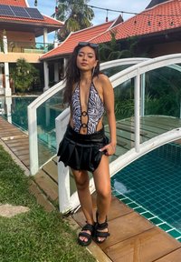 Costume da bagno con stampa a righe di zebra, gonne nere a pieghe sovrapposte e sandali neri chunky; ambientato in un contesto a bordo piscina.