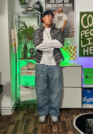 Conjunto informal que incluye una camisa a cuadros blanca y negra sobre una camiseta blanca, vaqueros azules holgados y zapatillas grises. Detalle de cadena en los vaqueros.