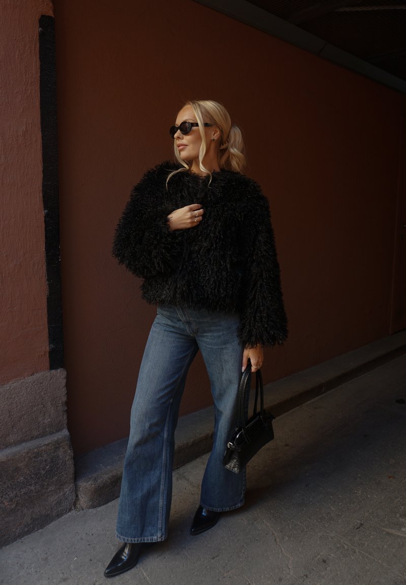 Musta, pörröinen tekoturkistakki, leveälahkeiset siniset farkut, terävät mustat kengät ja pieni musta käsilaukku. Yhtenäinen väri, pehmeä tekstuuri.