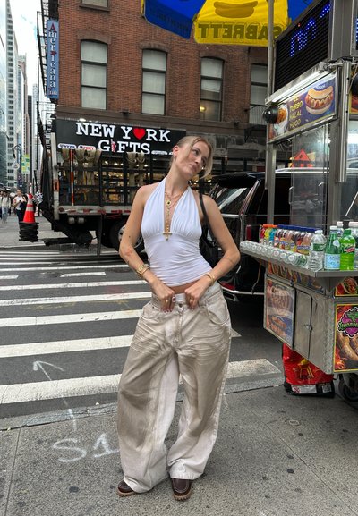 Pantalones anchos de color beige claro con una textura arrugada, combinados con untop halter blanco. Los accesorios incluyen collares en capas y pulseras.