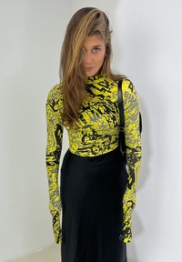 Long-sleeve top with a yellow and black abstract pattern, paired with a black skirt. The top has a fitted design and a high neckline.