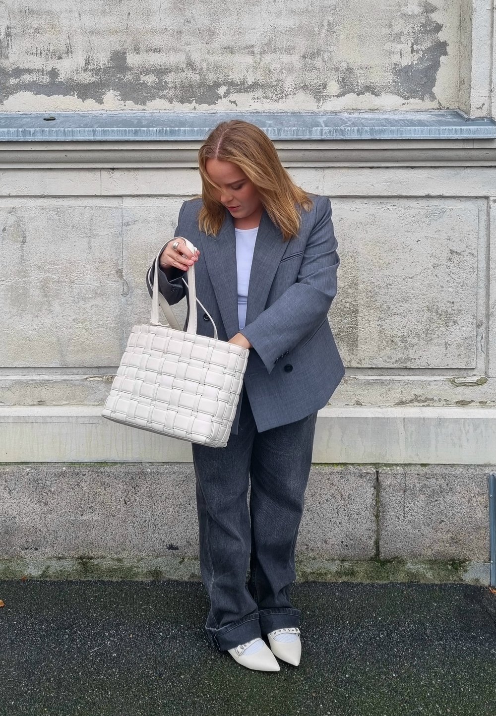 Siva tkana torba s dvostrukim ručkama, izrađena od sintetičkog materijala. Torba ima teksturirani, podstavljeni izgled. Model nosi sivi sako i traperice.