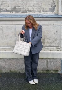 Siva tkana torba s dvostrukim ručkama, izrađena od sintetičkog materijala. Torba ima teksturirani, podstavljeni izgled. Model nosi sivi sako i traperice.