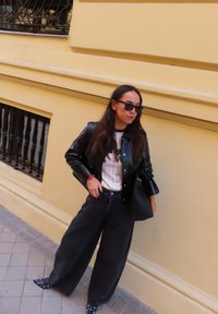 Černá lesklá bunda přes bílé pruhované tričko, široké černé kalhoty a špičaté černé boty s bílými puntíky. Pevná černá kabelka.