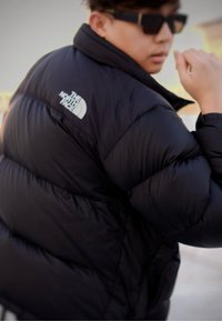 Μαύρο μπουφάν τύπου puffer με υψηλό γιακά, με επενδυμένη υφή και το λογότυπο της The North Face στον αριστερό ώμο.