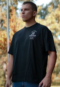 Schwarzes Baumwoll-T-Shirt mit kurzen Ärmeln und Rundhalsausschnitt. Vorne mit einem aufgedruckten Logo und Text in Pink.