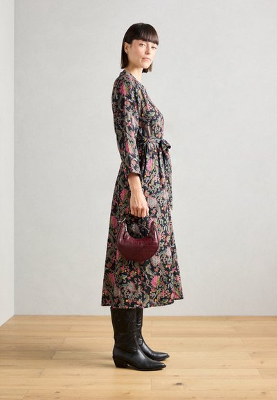 Vestido de flores de manga larga en negro, con coloridos patrones de cachemira y un lazo en la cintura; combinado con botas negras hasta el tobillo y un bolso burdeos.