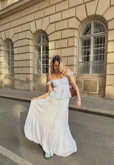 Blusa blanca, sin mangas y con detalles de botones, combinada con una falda blanca fluida. Tejido suave y texturizado con diseño en capas. Zapatillas casuales.