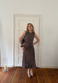 Bruine top met stippen en bijpassende rok, gecombineerd met naakte Mary Jane-schoenen en een zwarte handtas met een gemeleerde afwerking.