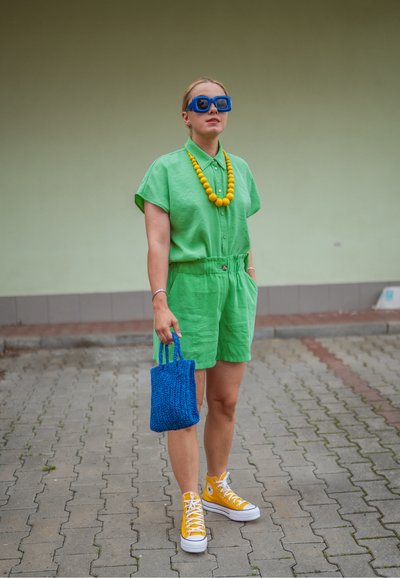 Conjunto de camisa de lino verde de manga corta y pantalones cortos, combinado con zapatillas amarillas, una bolsa de punto azul y un collar de cuentas amarillas.