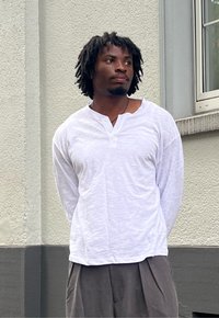 Camisa henley branca de manga longa com um tecido texturizado e botão de três, combinada com calças cinzas com pregas.